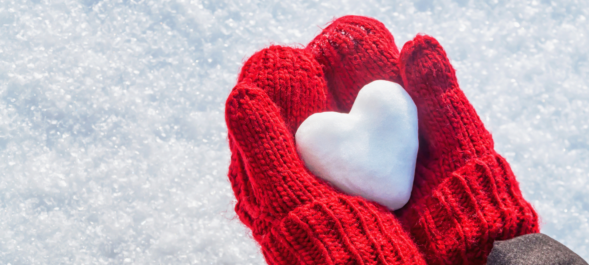Winterblues bekämpfen / rote Handschuhe halten ein Herz aus Schnee